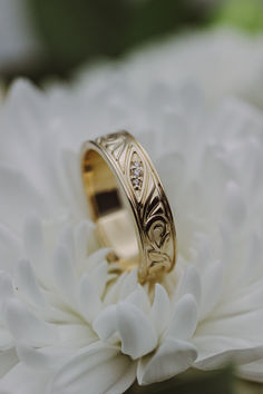 A 14K yellow gold mens' engagement band sits on a white chrysanthemum flower. This band features floral filigree details and three diamond accents. No Stone Wedding Ring, Men’s Wedding Ring Stone, Cool Guy Wedding Rings, Male Ring Band, Wedding Ring Band Men, Mens Wedding Ring Unique, Men’s Gold Wedding Band Engraved, Wedding Bands With Gemstones, Mens Wedding Rings Diamonds