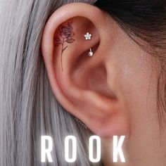 a woman with grey hair has a flower tattoo on her left side of the ear