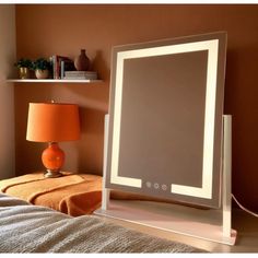 a mirror sitting on top of a bed next to a lamp and a night stand