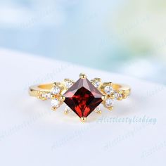 a gold ring with a red stone surrounded by white diamonds on a light blue background