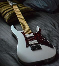 an electric guitar sitting on top of a bed next to a pillow and throw pillow