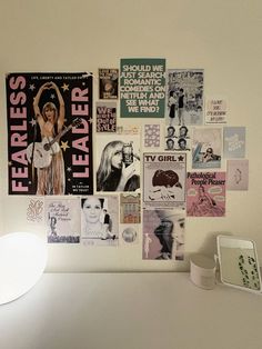 a white table topped with lots of posters on it's wall next to a lamp