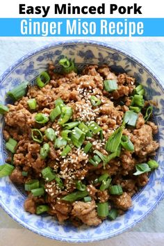 a blue and white bowl filled with meat and green onions, topped with sesame seeds