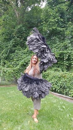 a woman is standing in the grass holding an ostrich feathered costume on her head