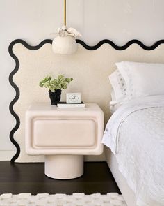 a white bed sitting next to a night stand on top of a wooden floor