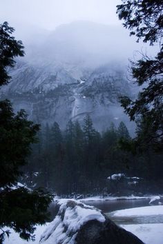 the mountain is covered in snow and surrounded by evergreen trees, with a river running through it