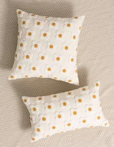 two white and yellow pillows sitting on top of a bed next to an orange pillow