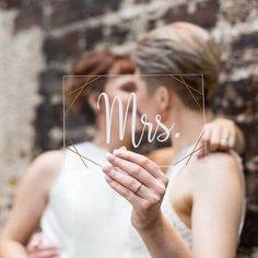 a bride and groom kissing behind a glass sign that says mr and mrs on it