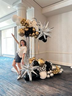 a woman is standing in front of some balloons and star decorations on the floor with her arms up