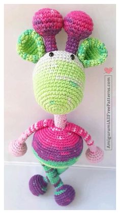 a crocheted giraffe is standing in front of a white wall with pink, green and purple stripes