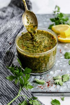 a spoon full of pesto sauce with lemons and parsley on the side