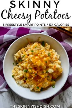 a white bowl filled with cheese potato casserole on top of a purple and white checkered table cloth