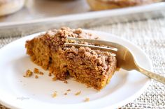 a piece of cake on a white plate with a fork in it and muffins in the background