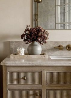 a vase with flowers sitting on top of a bathroom vanity