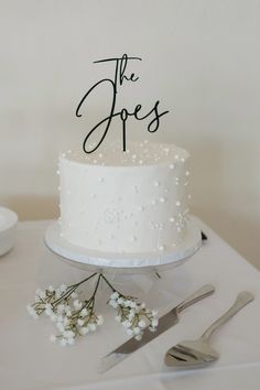 a white wedding cake with the word the jones on it and some silverware next to it