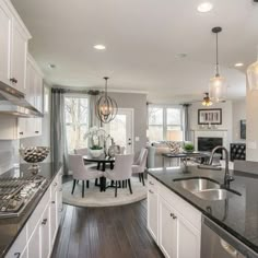 a kitchen with white cabinets and black counter tops next to a dining room table in front of a window