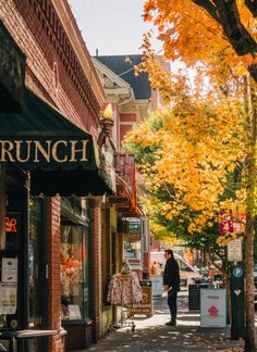 a man is walking down the street in front of a restaurant with autumn leaves on the trees