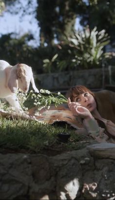 a woman laying in the grass next to a white dog and her puppy is looking at it