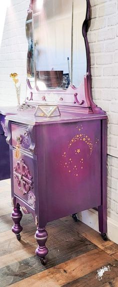 a purple vanity with an ornate mirror on it's side and drawers underneath the mirror