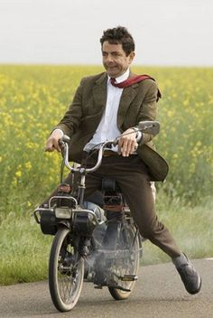 a man riding on the back of a motorcycle down a road next to a field