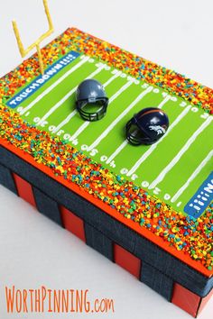 a cake shaped like a football field with two helmets on it and sprinkles