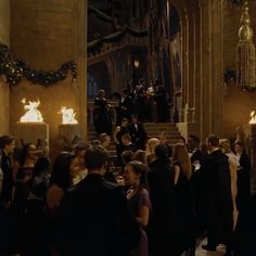 a large group of people standing around in a room with candles on the walls and stairs