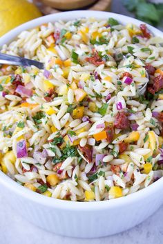 a white bowl filled with pasta salad next to a lemon