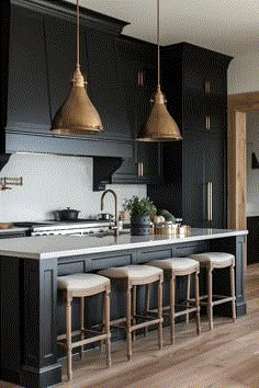 a kitchen with black cabinets and gold pendant lights hanging over the island countertop, along with four stools