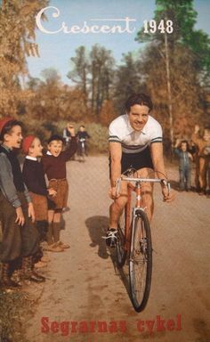 a man riding a bike down a dirt road with children watching from the sidelines