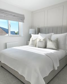 a bed with white sheets and pillows in a bedroom next to a window that looks out onto the ocean