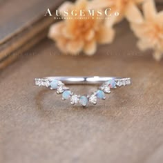 an opal and diamond ring sits on a wooden surface with flowers in the background