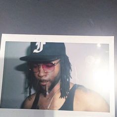 a polaroid photograph of a man with dreadlocks wearing a hat and sunglasses