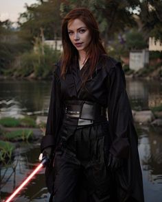 a woman dressed as darth vader standing in front of a pond with a lightsaben