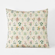 an embroidered pillow with flowers and leaves on the front, sitting on a white surface