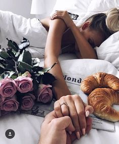 two people laying in bed with flowers and croissants next to each other