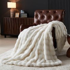 a brown leather chair with a white blanket on it's back in front of a black wall