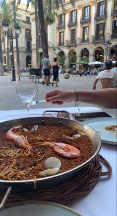 a large pan filled with food sitting on top of a table next to a glass of wine