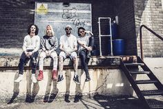 four people sitting on a ledge in front of a building