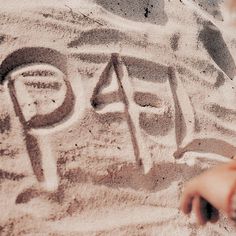 a child's hand writing on sand with the word peace written in it,