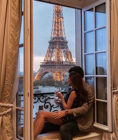 a woman sitting on a window sill looking out at the eiffel tower