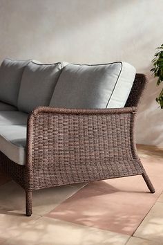 a wicker couch sitting on top of a tiled floor next to a potted plant