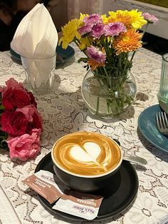 a cup of cappuccino on a table with flowers in vases and napkins