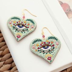 a pair of heart shaped earrings with an eye on the front and side, sitting on top of a white surface