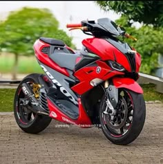 a red and black motorcycle parked on top of a brick road in front of trees