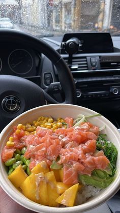 a person is holding a bowl of food in their hand while inside a car with the steering wheel behind them