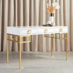 a white desk with two drawers and a vase on the top, in front of a curtained window