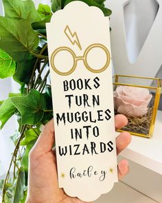 a hand holding up a bookmark with harry potter's glasses on it and the words, books turn muggles into wizards