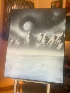 an easel with a painting on it that has mountains in the background and a full moon