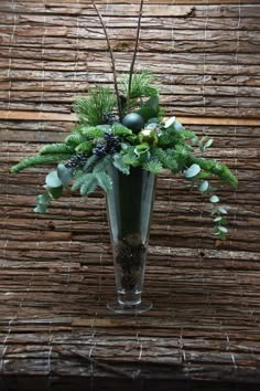 a vase filled with flowers and greenery on top of a wooden table next to a bamboo wall