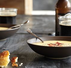 a bowl of soup on a table next to a plate with bread and syrup in it